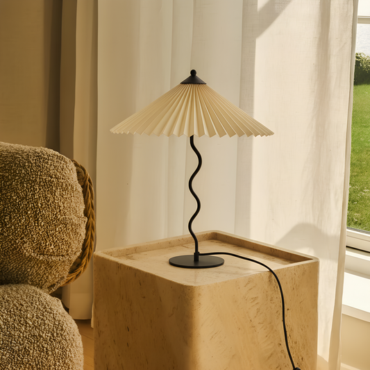 Table lamp with pleated shade on a wooden side table by a window