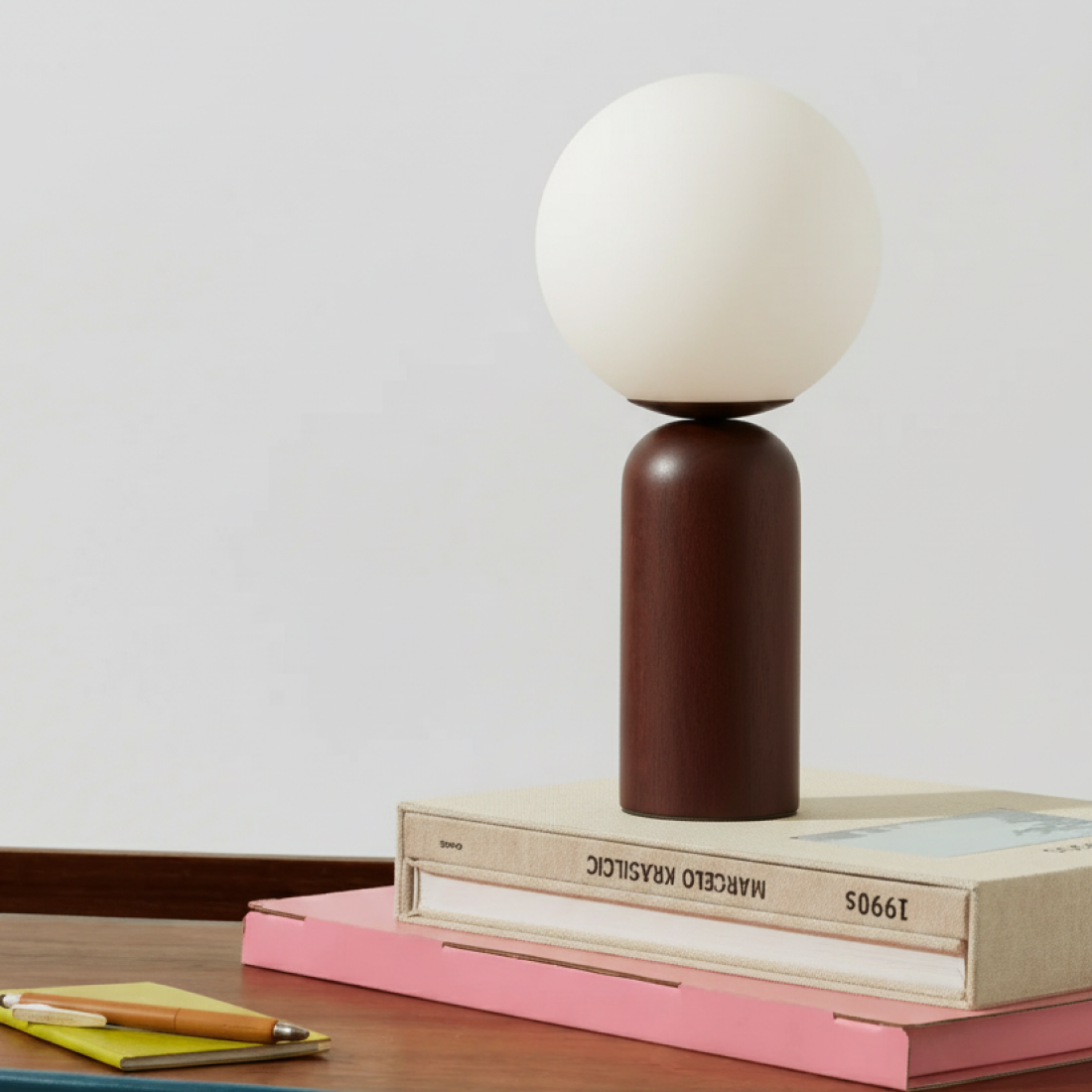 Table lamp with a round white shade on a brown cylindrical base, placed on books on a wooden surface.